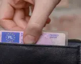Dłoń wkłada do czarnego portfela polskie prawo jazdy. Widoczny jest numer blankietu dokumentu.