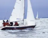 Un voilier nommé "FUN" navigue sur une mer agitée, avec des personnes à bord profitant de la navigation.