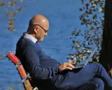 Mężczyzna w okularach siedzi na ławce nad jeziorem, pracując na laptopie. Planuje swoje ubezpieczenie emerytalne, ciesząc się spokojem natury.