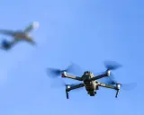 Drohne im Flug, während ein Flugzeug im Hintergrund verschwimmt. Informiere dich über Länder, in welchen Ländern Drohnen verboten sind, bevor du abhebst.