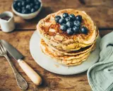 Pile de pancakes au levain garnis de myrtilles, sur une assiette, avec une fourchette et un couteau.