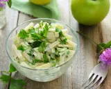 Frischer Kohlrabi Salat mit Petersilie in einer Glasschüssel, garniert mit einer lila Blume und grünen Äpfeln auf Holztisch.