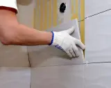 Man con guantes coloca una baldosa nueva sobre un alicatado existente.