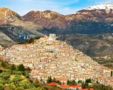 Un pittoresco borgo calabrese si aggrappa a una collina, con case in pietra e tetti rossi che si estendono fino alle montagne innevate.