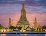 Il **tempio dell'alba Bangkok** (Wat Arun) si erge maestoso al tramonto, con le sue guglie dorate che brillano contro un cielo rosa e viola.