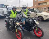 Dos motoristas con chalecos reflectantes y cascos posan con sus motos. Uno hace un gesto de "pulgar arriba". ¡Listos para la aventura en su a1 de moto!