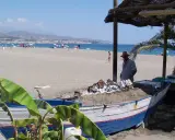 Ein Mann grillt Fisch auf einem Strand in Torre del Mar. Im Hintergrund das Meer und Berge.