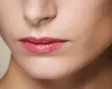 Labbra sottili e lucide con un tocco di gloss rosa, che catturano la luce.