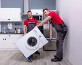 Dwóch mężczyzn w roboczych ubraniach przewozi pralkę na wózku. Czy można przewozić pralkę na leżąco? To pytanie zadaje sobie wielu przy przeprowadzce.