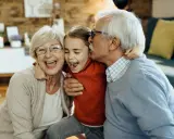 Una niña ríe mientras su abuelo le da un beso y su abuela la abraza. Así de felices los abuelos son.