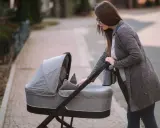 Młoda mama pochyla się nad szarym wózkiem dla dzieci, gotowa na spacer.