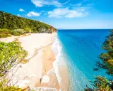 En orörd albanien strand med turkost vatten, vit sand och gröna kullar. En liten flod rinner ut i havet.