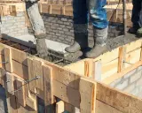 Vertiendo hormigón en el encofrado de construcción. Obreros con botas embarradas supervisan el proceso.