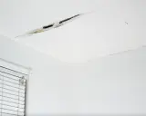 Widoczne pęknięcia na łączeniu sufitu i ściany, świadczące o problemach z konstrukcją lub wilgocią.