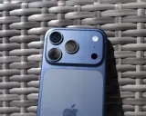 Niebieski iPhone 11 z potrójnym aparatem z tyłu, leżący na plecionej powierzchni.
