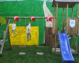 Un niño observa un columpio y un tobogán azul, parte de unos juegos medievales para niños, con un mural de fondo.