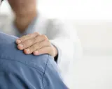Dłoń lekarza na ramieniu pacjenta. Czy do psychiatry potrzebne jest skierowanie? Wsparcie i troska w gabinecie lekarskim.