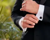 A man fastens his black cufflinks on his white shirt cuffs, completing his tux.