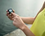 Dłoń dotyka ekranu małego urządzenia, które działa jak krokomierz w telefonie, pokazując liczbę kroków.