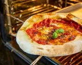 Leckere Pizza Margherita mit frischem Basilikum wird im Backofen gebacken. Der Teig ist goldbraun, die Tomatensauce blubbert.