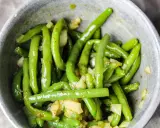 En skål med glansiga, gröna haricots verts blandade med bitar av vitlök och kryddor.