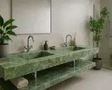 Luksusowy blat do łazienki z kamienia w odcieniu zieleni z żyłkami. Dwie umywalki, chromowane baterie, lustro i rośliny tworzą elegancką przestrzeń.