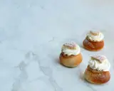 Tre semlor utan mandelmassa, toppade med vispgrädde och pudersocker, ligger på ett marmorbord.