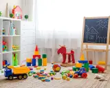 Kolorowy pokój zabaw dla dzieci w domu. Na dywanie rozrzucone klocki, ciężarówka, traktorek, huśtawka-łoś i tablica z rysunkiem domku.