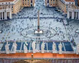 Vue aérienne de la **place du Vatican**, avec son obélisque central, ses fontaines et une foule de visiteurs.