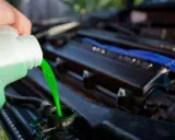 Mano vierte líquido refrigerante verde brillante en el radiador de un coche. Guía para saber como cambiar el liquido refrigerante.