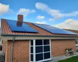 Ett tegelhus med solpaneler på taket, redo att generera egen energi. Blå himmel med vita moln.