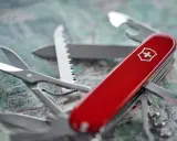 Czerwony scyzoryk z białym krzyżem na tle mapy. Gotowy na każdą podróż, nawet tę z bagażem rejestrowanym.