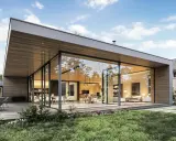 Maison moderne avec une extension sur toit plat existant, offrant de grandes baies vitrées donnant sur un jardin verdoyant.