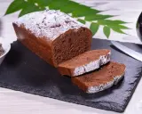 Ein saftiger Schokoladenkuchen, bestäubt mit Puderzucker, bereit für ein köstliches rotweinkuchen rezept. Daneben Schokoladendrops und ein Glas Rotwein.