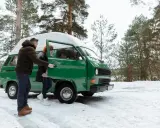 Para zimowa przygoda: czy kamper jest samochodem osobowym? Para wysiada z zielonego kampera na zaśnieżonej polanie w lesie.