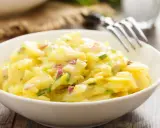 Schüssel mit cremigem Kartoffelsalat ohne Mayo, garniert mit roten Zwiebeln und Schnittlauch. Ein Klassiker, der immer schmeckt!