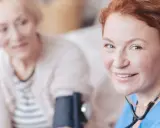 Uśmiechnięta pielęgniarka z rudymi włosami mierzy ciśnienie starszej kobiecie. Dopegyt w ciąży jest bezpieczny dla matki i dziecka.