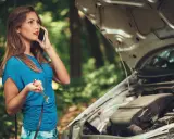 Mujer llama por teléfono con una llave inglesa en la mano, preguntando por qué se me para el coche en marcha. El capó del coche está abierto.