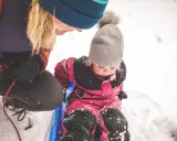 En vuxen drar ett barn på en pulka i snön. Ett perfekt exempel på friluftsliv barn.