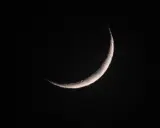Eine schmale Mondsichel leuchtet im dunklen Nachthimmel. Sie erinnert an den Beginn von Ramadan, wann die Zeit des Fastens beginnt.