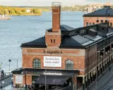 Fotografiska Stockholm vid vattnet, med en båt i förgrunden och en stadssilhuett i bakgrunden.