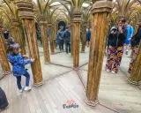 Niños exploran un laberinto de espejos con columnas doradas, creando un divertido juego de "praga con niños" y reflejos infinitos.