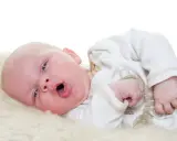 Baby mit offenem Mund, vielleicht husten. Was tun? Ein süßer kleiner Mensch auf weichem Fell.