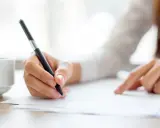 Dłoń pisze piórem, przygotowując frazy do eseju "za i przeciw". Obok filiżanka kawy.