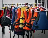 Chalecos salvavidas de varios colores, como naranja, amarillo y azul, colgados en perchas. Listos para la aventura, estos chalecos son de epis categoria 2.