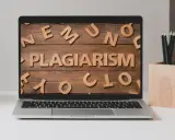 Laptop z napisem "PLAGIARISM" ułożonym z drewnianych liter na tle desek.