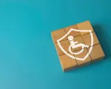 Drewniane klocki tworzą tarczę z symbolem osoby na wózku inwalidzkim. To symbol tego, co daje orzeczenie o niepełnosprawności – wsparcie i ochronę.