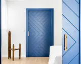 Puertas azules interiores con diseño geométrico y tiradores de madera. Una silla de madera antigua destaca junto a una de las puertas.