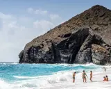 Sonniger Almería Urlaub: Menschen genießen den Strand und das Meer vor einer imposanten Felsformation.