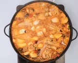 Un suquet de peix burbujeante en una paellera, con trozos de pescado, patatas, gambas y mejillones en una salsa naranja.